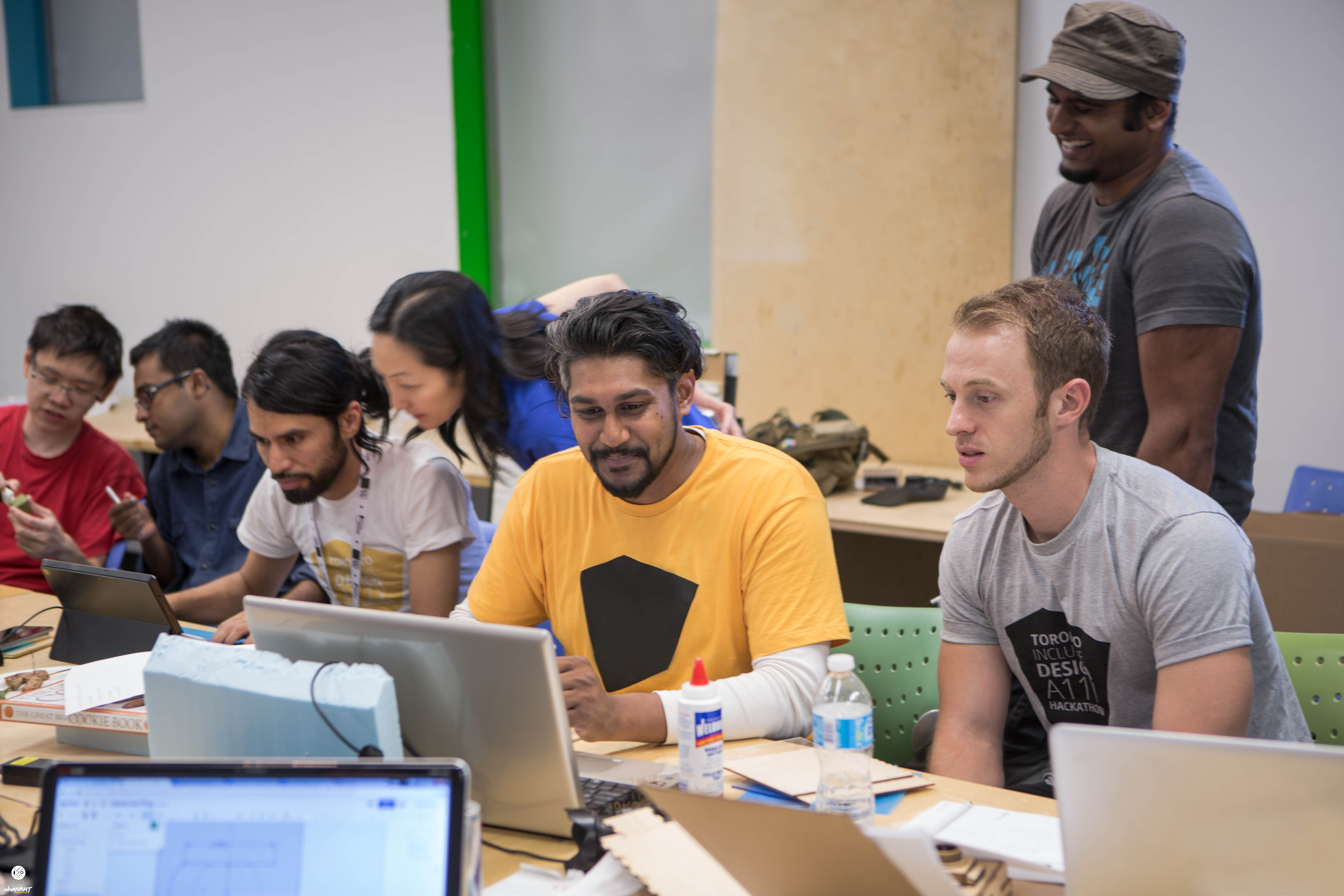 Group of seven individuals discussing a project and looking at their laptor screens
